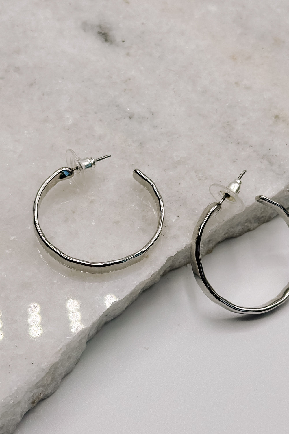 Close up view of the Layla Silver Hammered Hoop Earring which features medium open silver hammered hoops