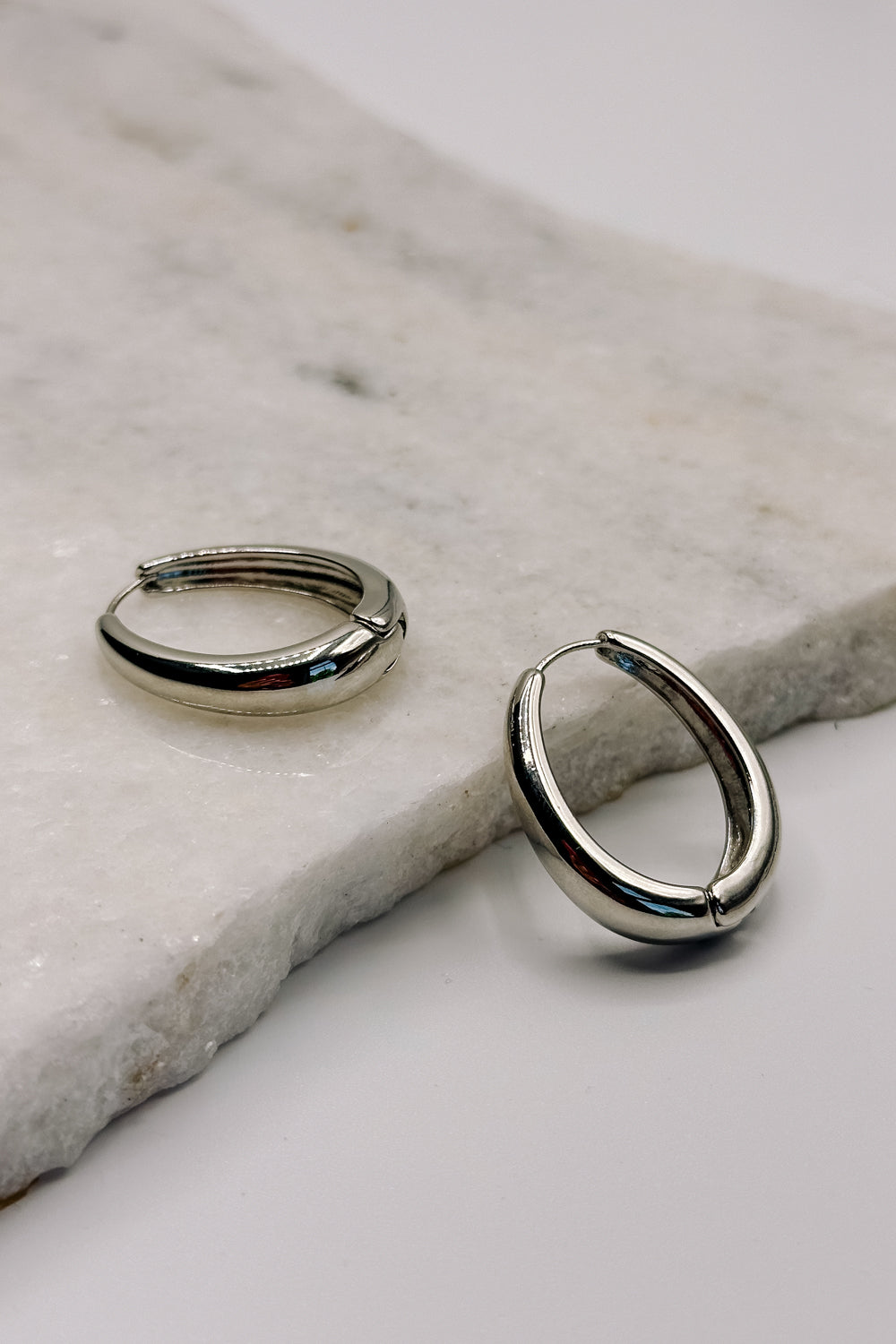 Flat lay view of the Luna Silver Oval Hoop Earring. the earring features silver medium open hoops