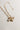 Image shows gold necklace chain with white clover charm, heart charm, and rope bow charm. Shown against a white background.