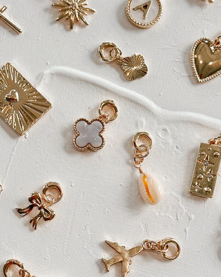 Image shows assorted charms against a white background. Charms pictured include white clover, gold clover, heart, star medallion, airplane, black clover, bow, cowboy boy, heart medallion, and starbust.