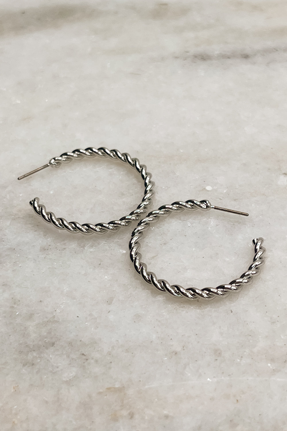 Earrings shown lying on a neutral background. The Valentina Hoops are silver, rope hoops. Alternate view.