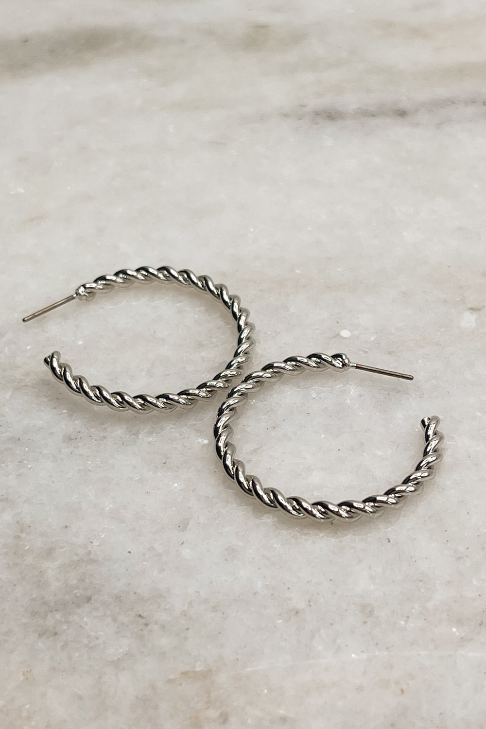 Earrings shown lying on a neutral background. The Valentina Hoops are silver, rope hoops.