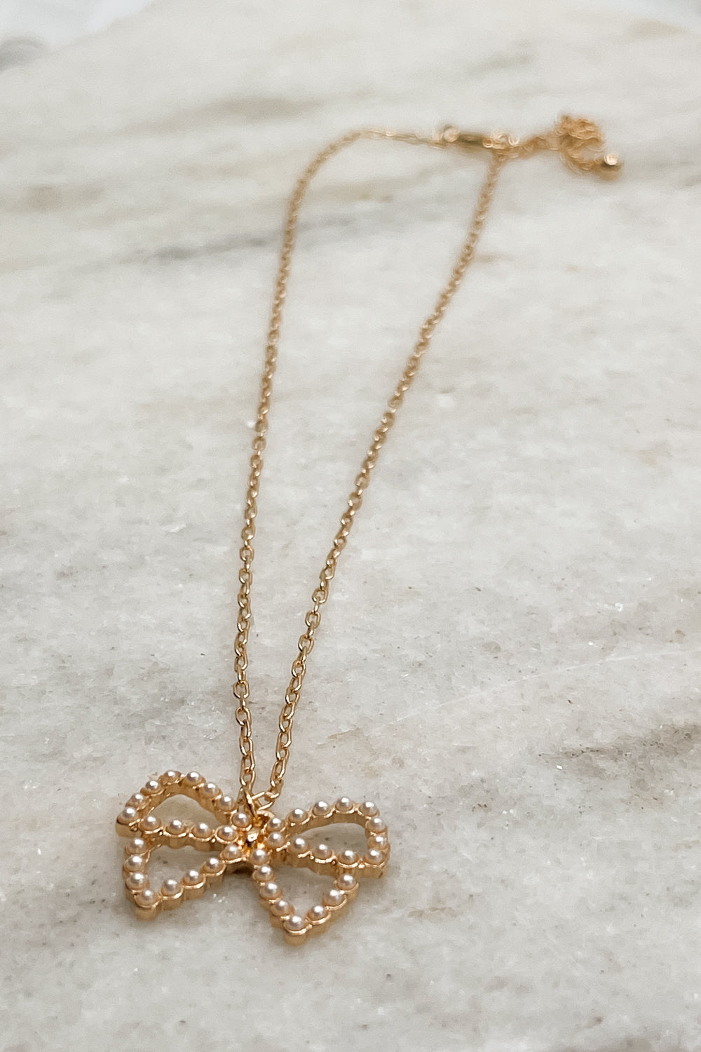 Close up of Violet Pearl Bow Gold Necklace that is adjustable with a pearl bow detail, beautifully paired with any outfit. 