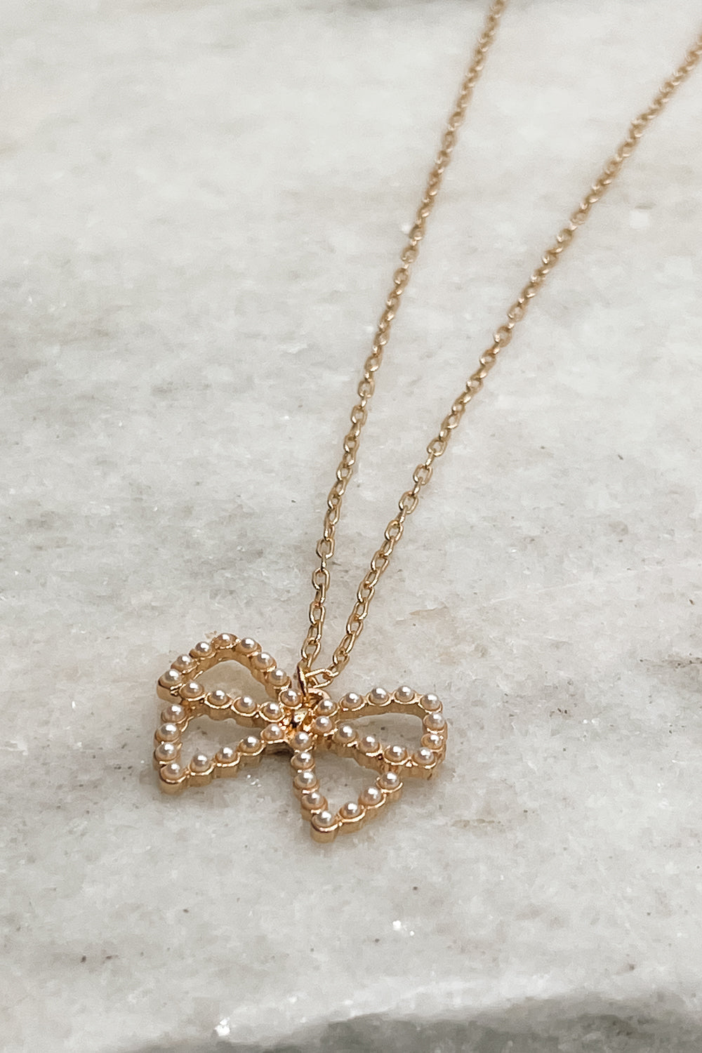 Close up of Violet Pearl Bow Gold Necklace that is adjustable with a pearl bow detail, beautifully paired with any outfit.