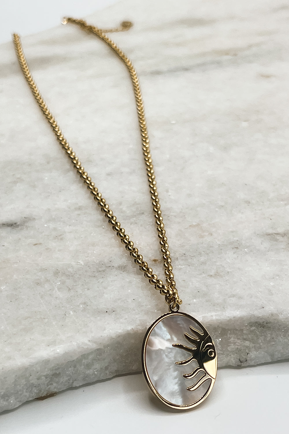 The Soleil Necklace is seen against a neutral background. The charm is opalescent and has a sun design.