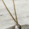 The Soleil Necklace is seen against a neutral background. The charm is opalescent and has a sun design.