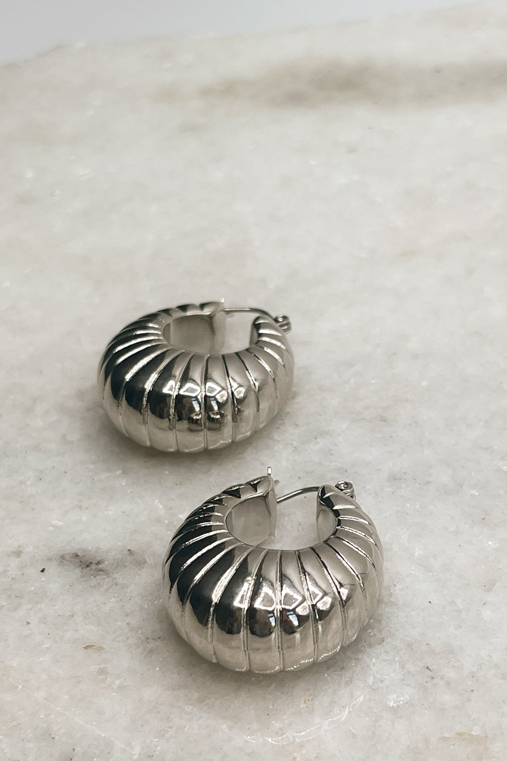 The Ellory Croissant Hoop Earrings are seen laying on a neutral background.