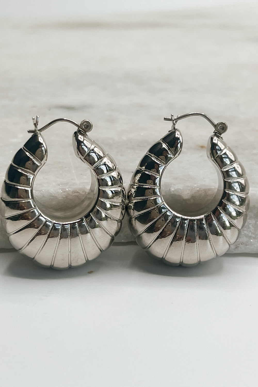The Ellory Croissant Hoop Earrings are seen laying on a neutral background.
