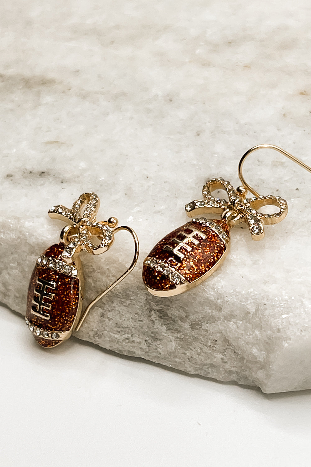  Close up of Callie Brown Rhinestone Football Earrings that are dangle earrings with rhinestone bows and footballs.