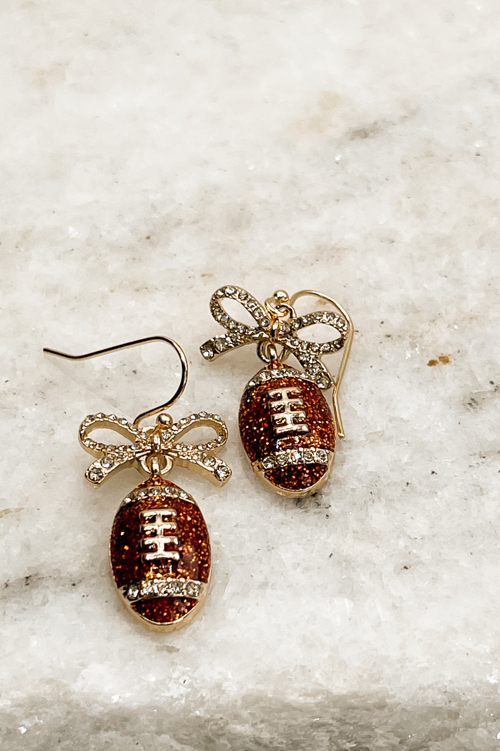 Close up of Callie Brown Rhinestone Football Earrings that are dangle earrings with rhinestone bows and footballs.