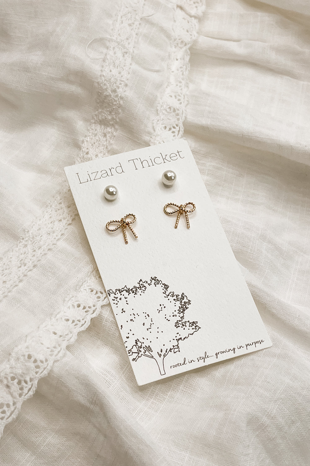 The earring set is seen on a neutral background. The two pairs of earrings are fastened to the card they are packaged in. 