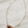 Image shows the Abby Gold Football Pendant Necklace against a marble background. Necklace features thin gold chain and a sparkly brown football pendant with pearl and gold detailing.