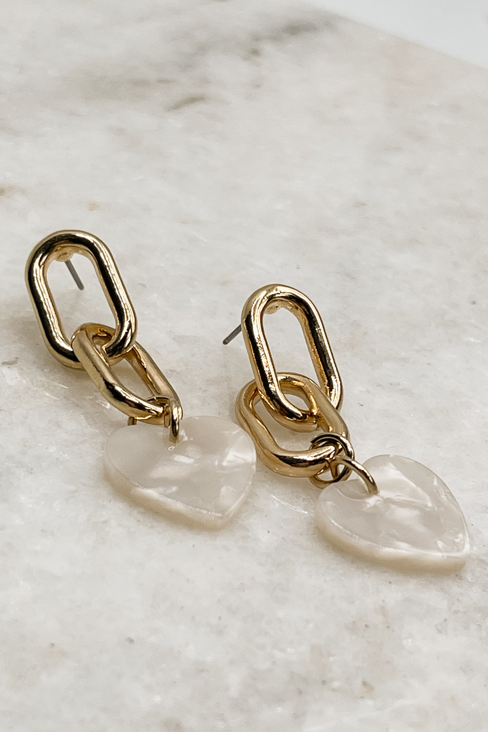 Image shows the Alia Gold Link & White Heart Earrings against a white background. Earrings have two gold chain links with a white marble heart pendant.