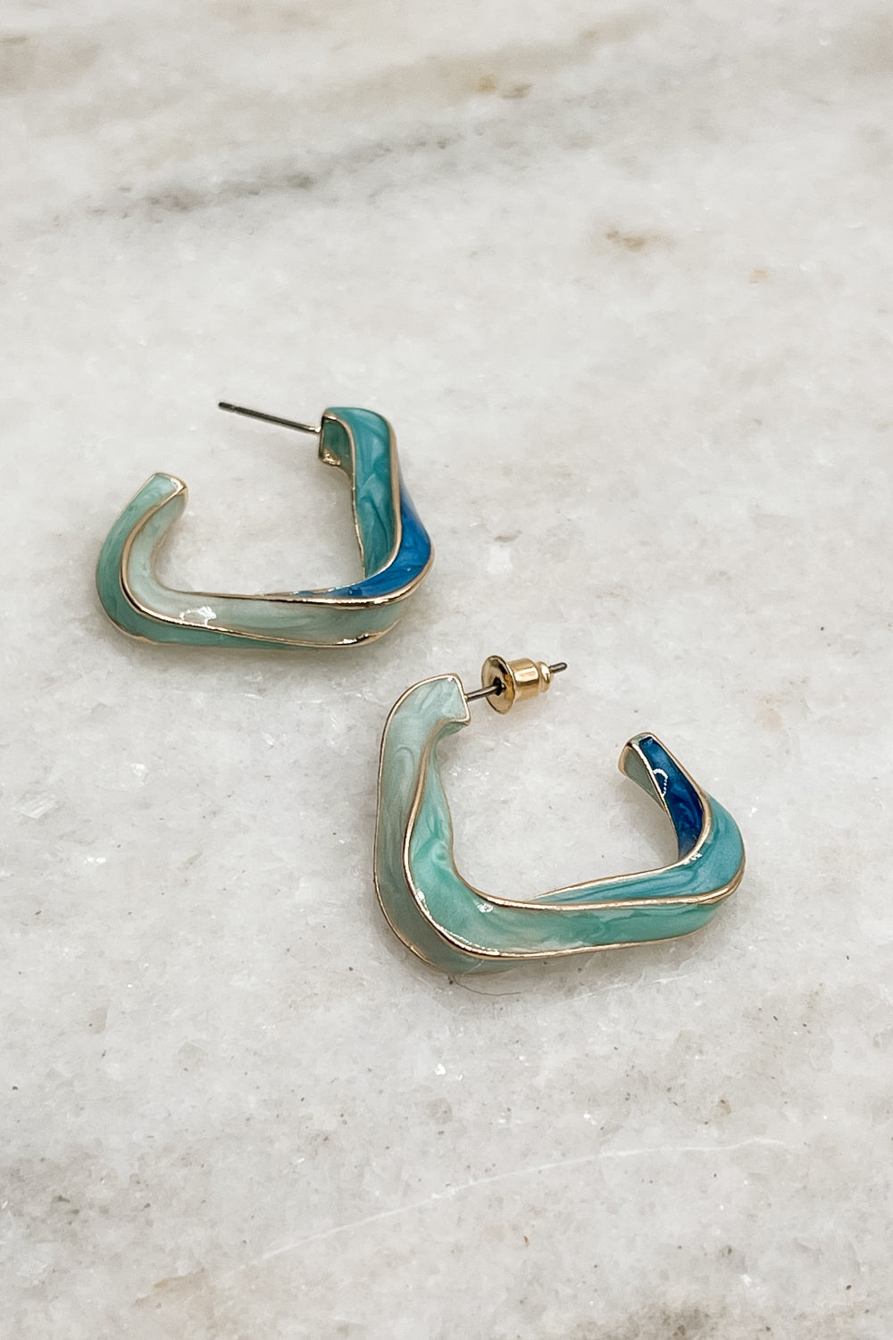 The Greyson Earrings are shown. They are gold and blue twisted hoops in a geometric shape.