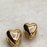 The Raine Earrings are shown against a neutral background. They are gold heart-shaped studs.