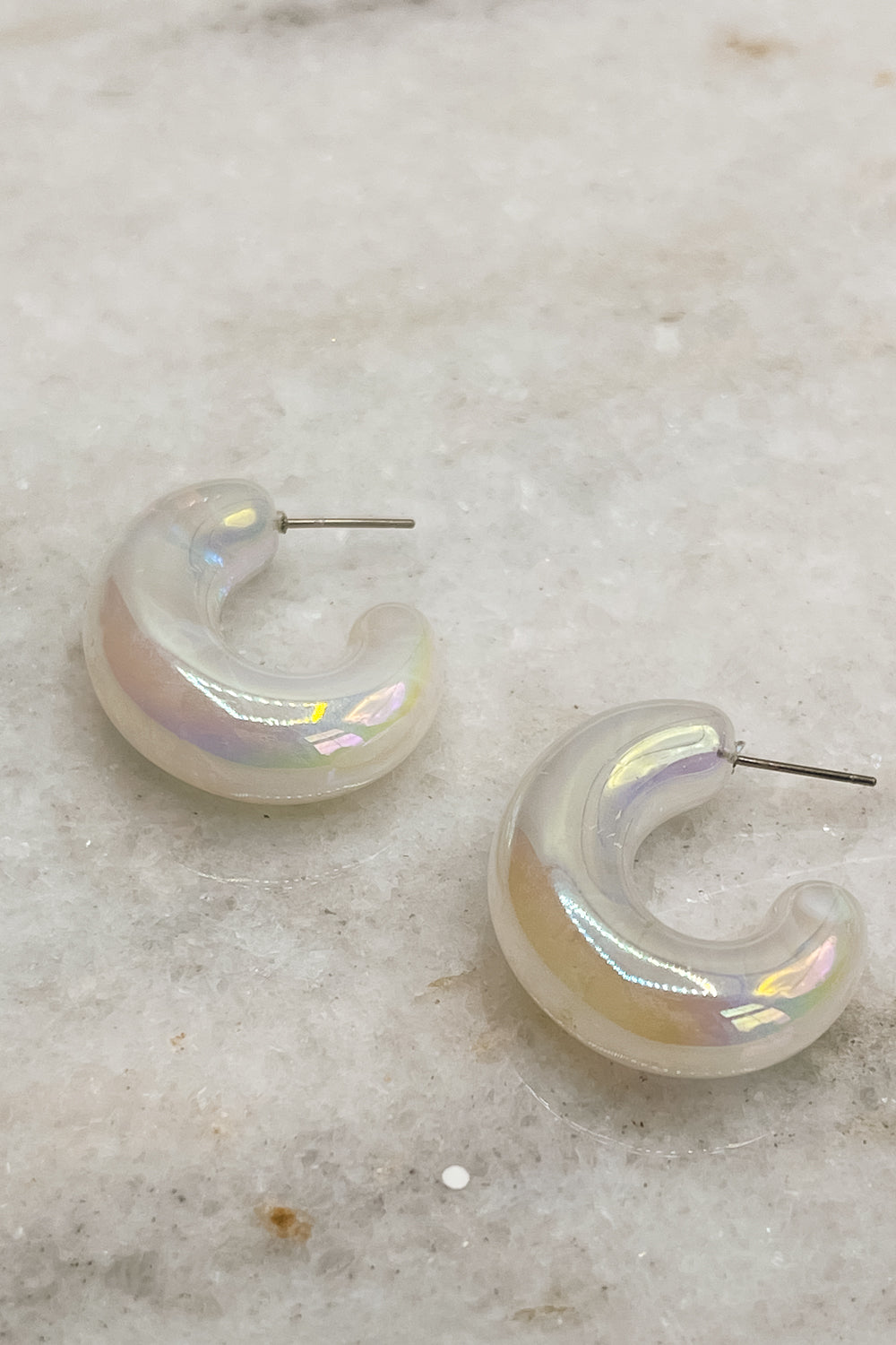 Image shows the Calista Iridescent Scoop Hoop Earrings against a white marble background. Earrings have white iridescent material with open hoop shape.