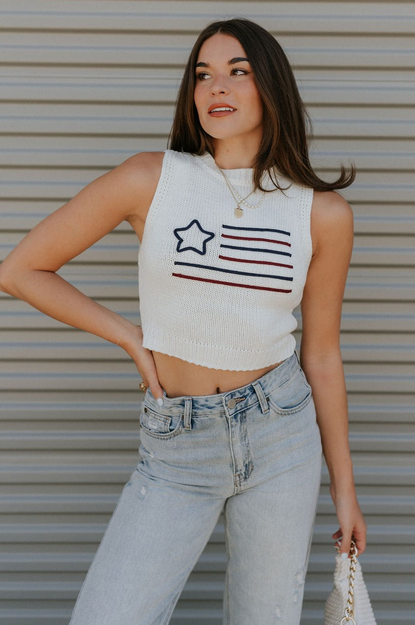 front view of female model wearing the Star America Flag Cream Knit Tank which features Cream Knit Fabric, Round Neckline, Sleeveless and Dark Red and Navy American Flag Stitch Design