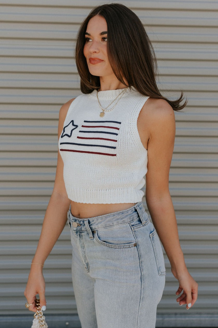 side view of female model wearing the Star America Flag Cream Knit Tank which features Cream Knit Fabric, Round Neckline, Sleeveless and Dark Red and Navy American Flag Stitch Design