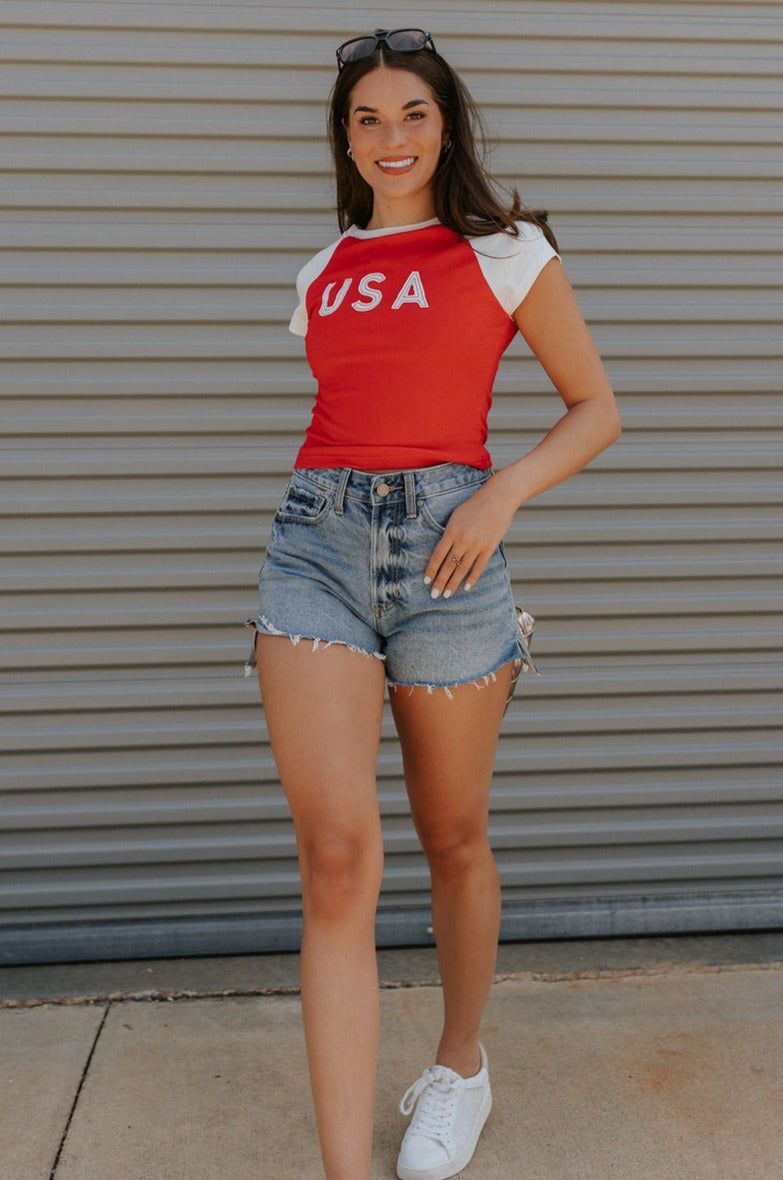 Full body view of female model wearing the USA Red & White Short Sleeve Top which features Red and White Lightweight Fabric, Color Block Pattern, Round Neckline, Short Sleeves and USA graphic stitch design