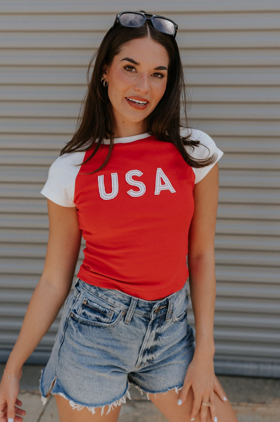 front view of female model wearing the USA Red & White Short Sleeve Top which features Red and White Lightweight Fabric, Color Block Pattern, Round Neckline, Short Sleeves and USA graphic stitch design