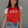 front view of female model wearing the USA Red & White Short Sleeve Top which features Red and White Lightweight Fabric, Color Block Pattern, Round Neckline, Short Sleeves and USA graphic stitch design