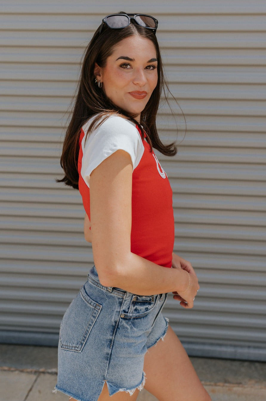 side view of female model wearing the USA Red & White Short Sleeve Top which features Red and White Lightweight Fabric, Color Block Pattern, Round Neckline, Short Sleeves and USA graphic stitch design