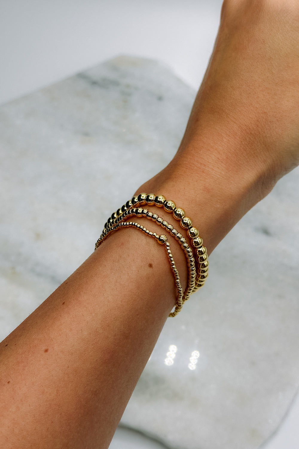 Image shows Aubrey Gold 4mm Beaded Water Resistant Bracelet worn on model's wrist with two other bracelets.