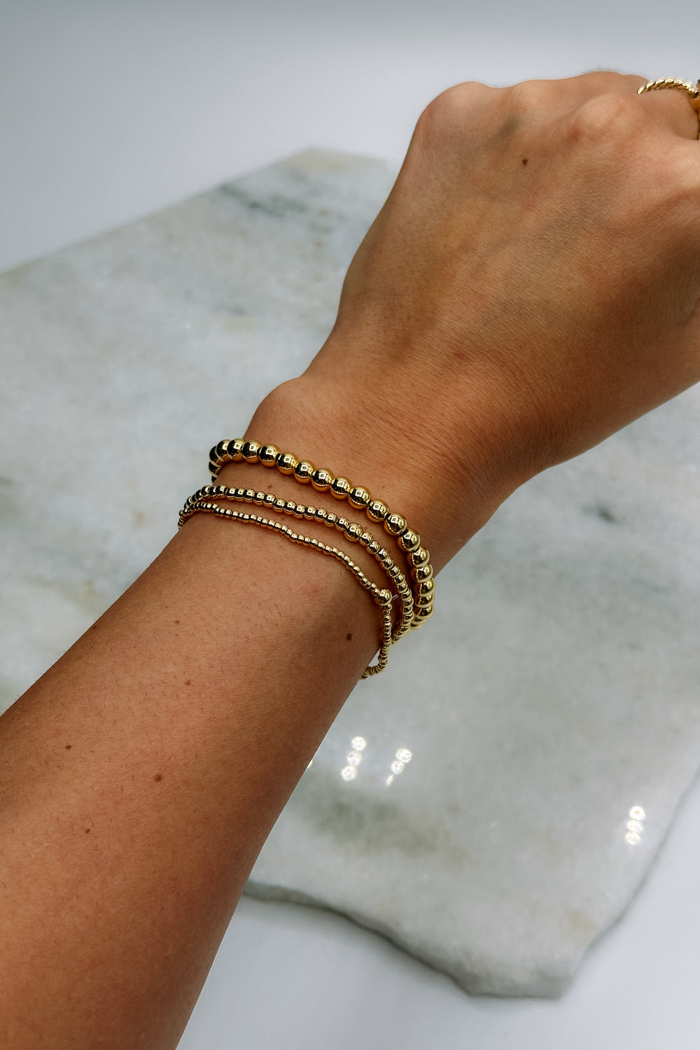 Image shows Clara Gold 6mm Beaded Water Resistant Bracelet on a model's wrist with 2 other bracelets.