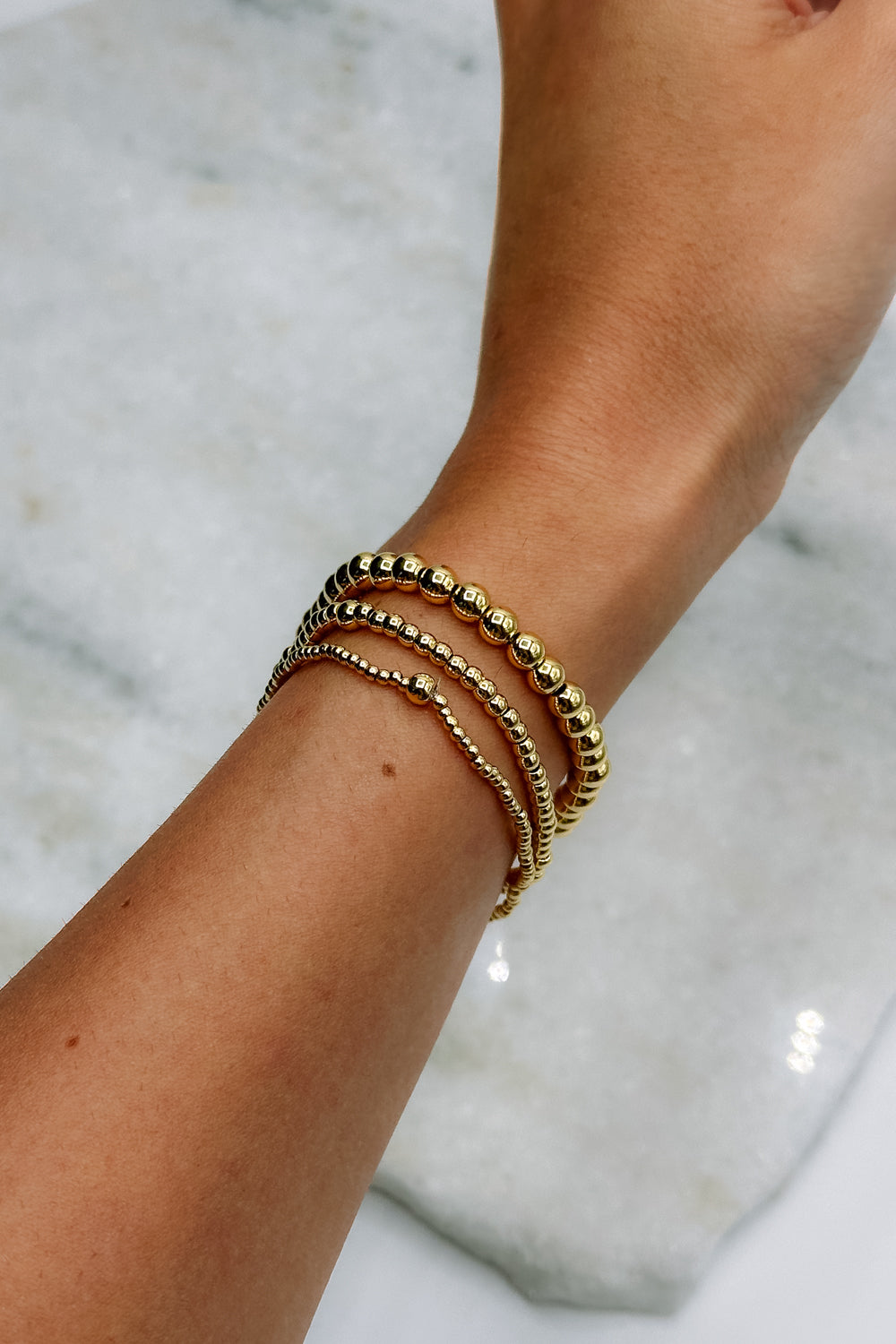 Image shows Jane Gold 2mm Beaded Water Resistant Bracelet on model's wrist with two other bracelets.