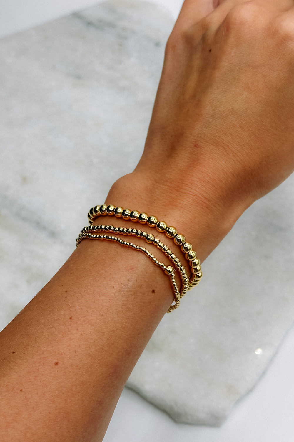 Image shows Jane Gold 2mm Beaded Water Resistant Bracelet on model's wrist with two other bracelets.