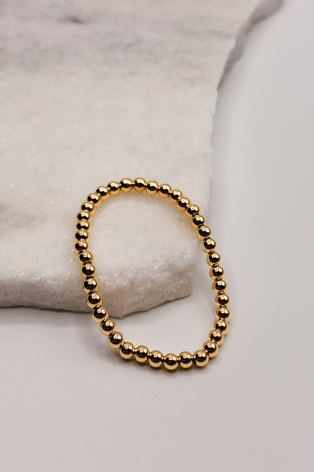 Image shows Clara Gold 6mm Beaded Water Resistant Bracelet against a white marble background.