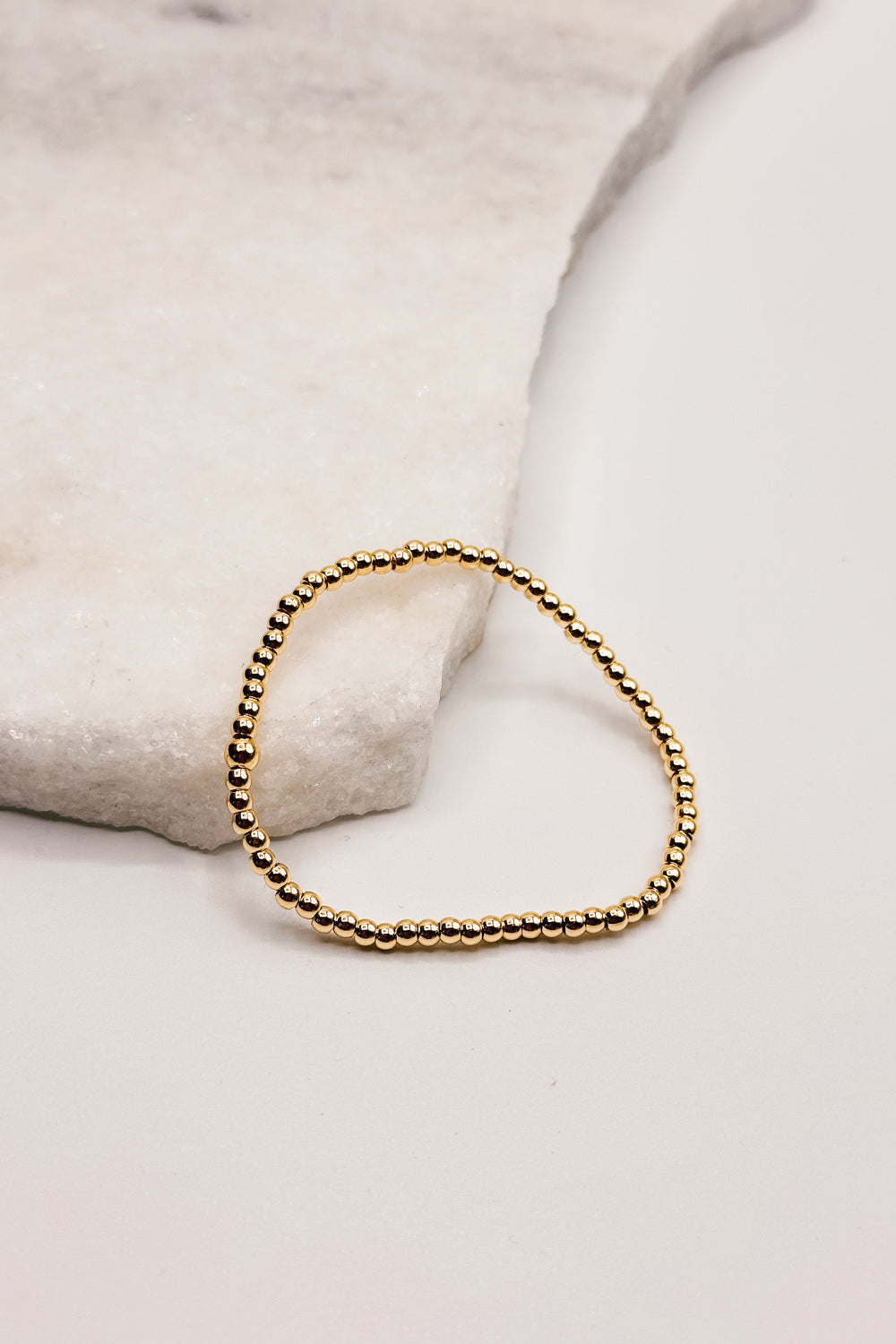 Image shows Aubrey Gold 4mm Beaded Water Resistant Bracelet against a white marble background.