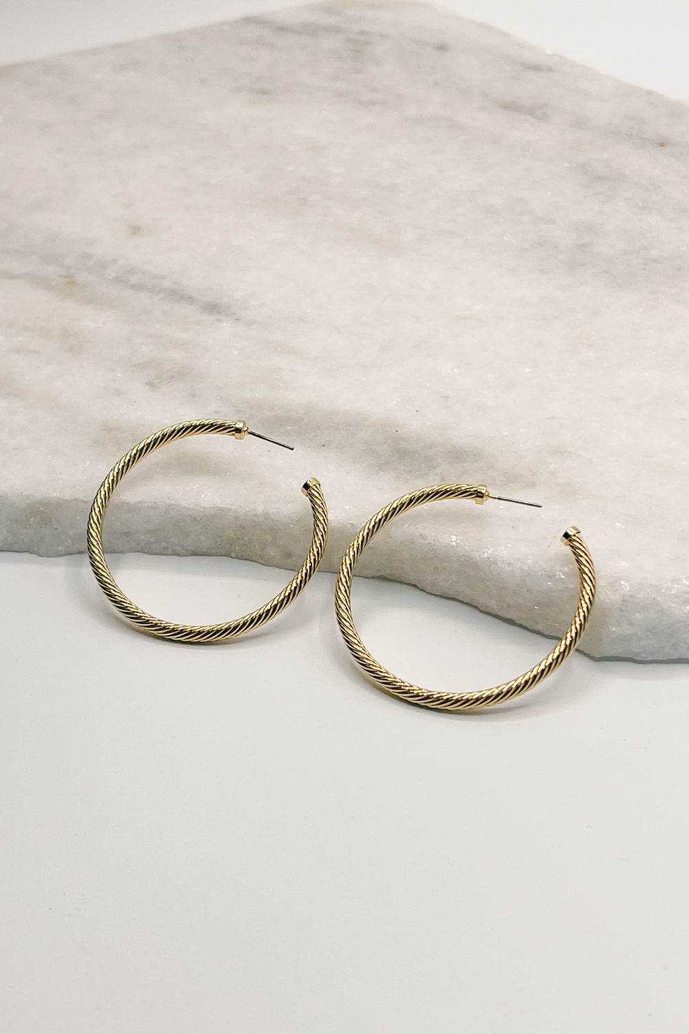 flat lay view of the Eliza Gold Dipped  Ribbed Hoop Earring. the earring features open medium gold dipped ribbed thin hoops