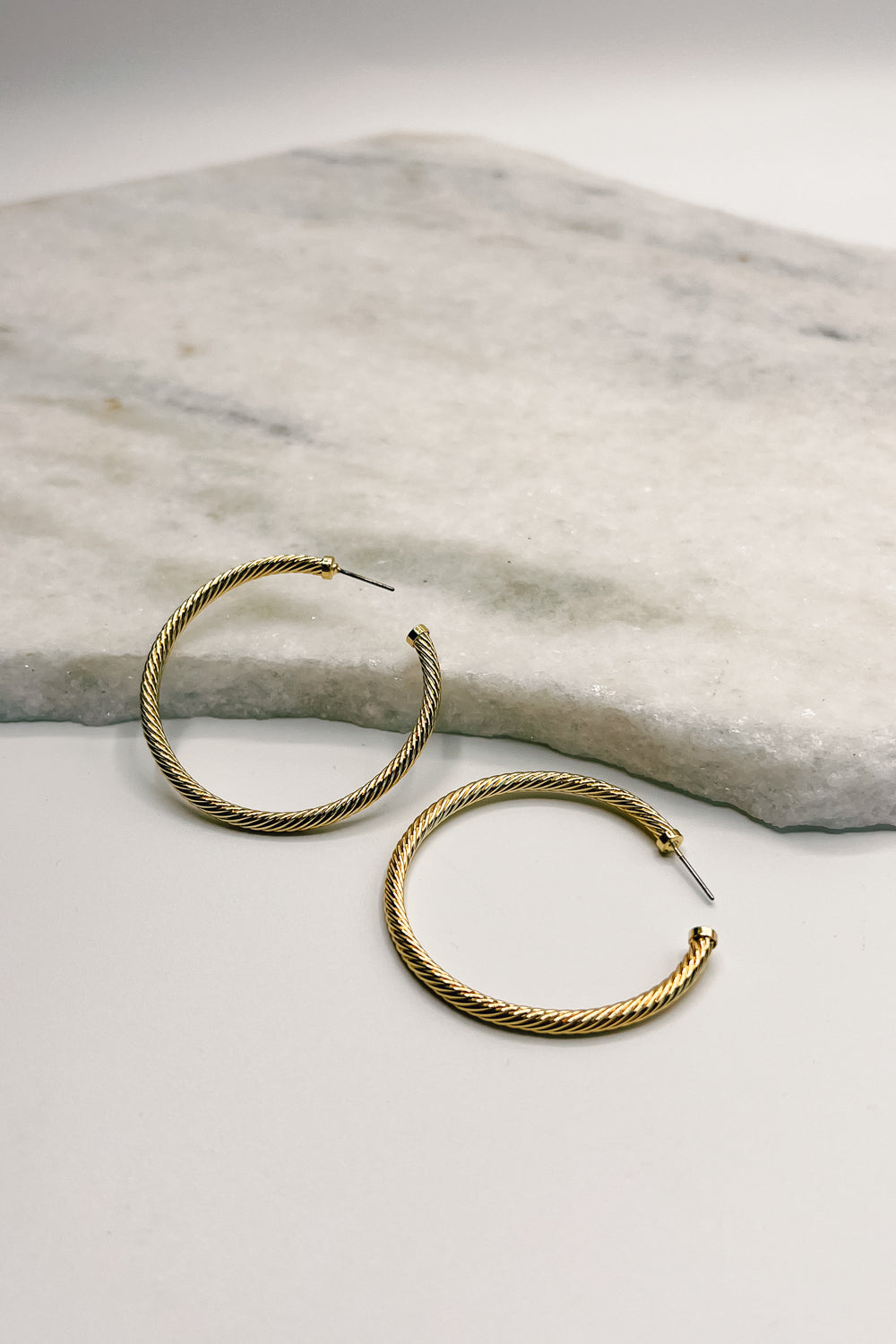 flat lay view of the Eliza Gold Dipped Ribbed Hoop Earring. the earring features open medium gold dipped ribbed thin hoops
