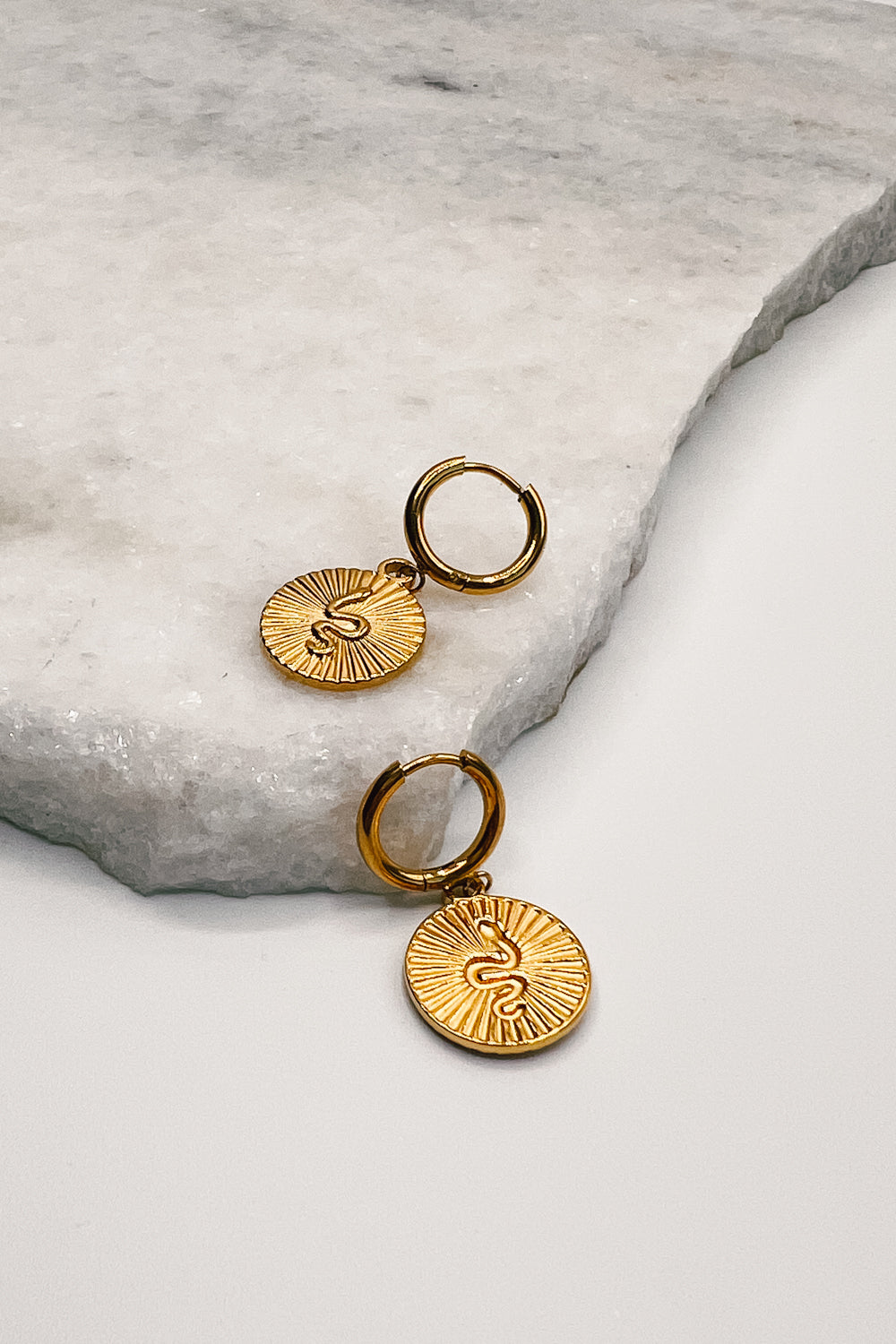 flat lay view of the Snake Ribbed Gold Circle Huggie Earrings which features gold huggies with snake ribbed circle medallions