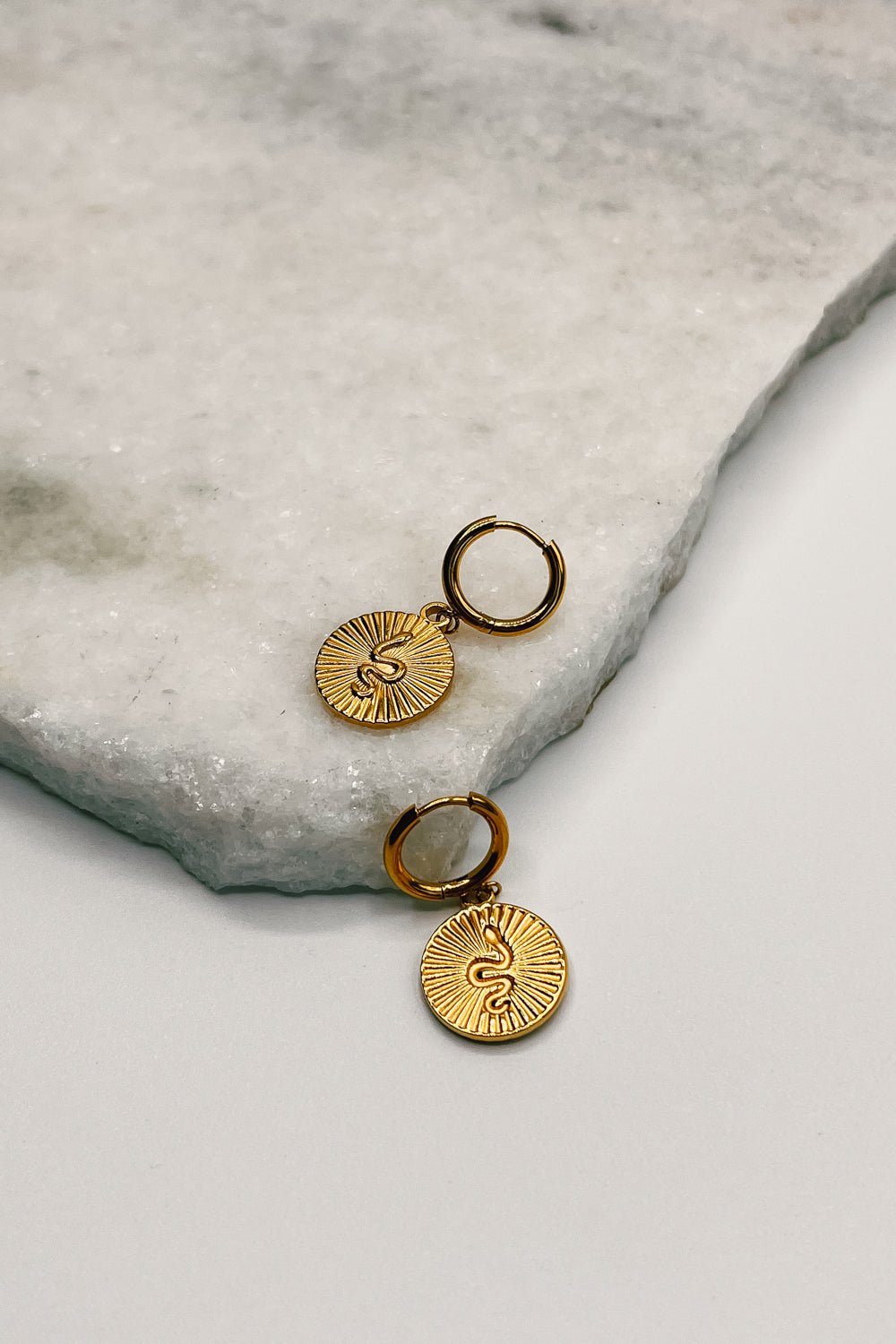 flat lay view of the Snake Ribbed Gold Circle Huggie Earrings which features gold huggies with snake ribbed circle medallions