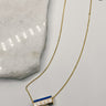 Image shows Love White & Blue Cylinder Necklace against a white background. Necklace has 6 sided cylinder - 2 white sides that say love, 2 blue sides, and 2 black sides with a geometric design.