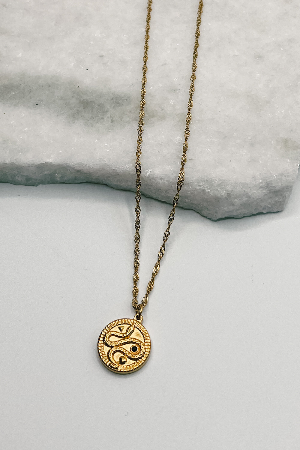 Image shows Samara Gold Snake Medallion Necklace against a white background. Necklace has a gold chain and a circle gold pendant that has a snake on it.