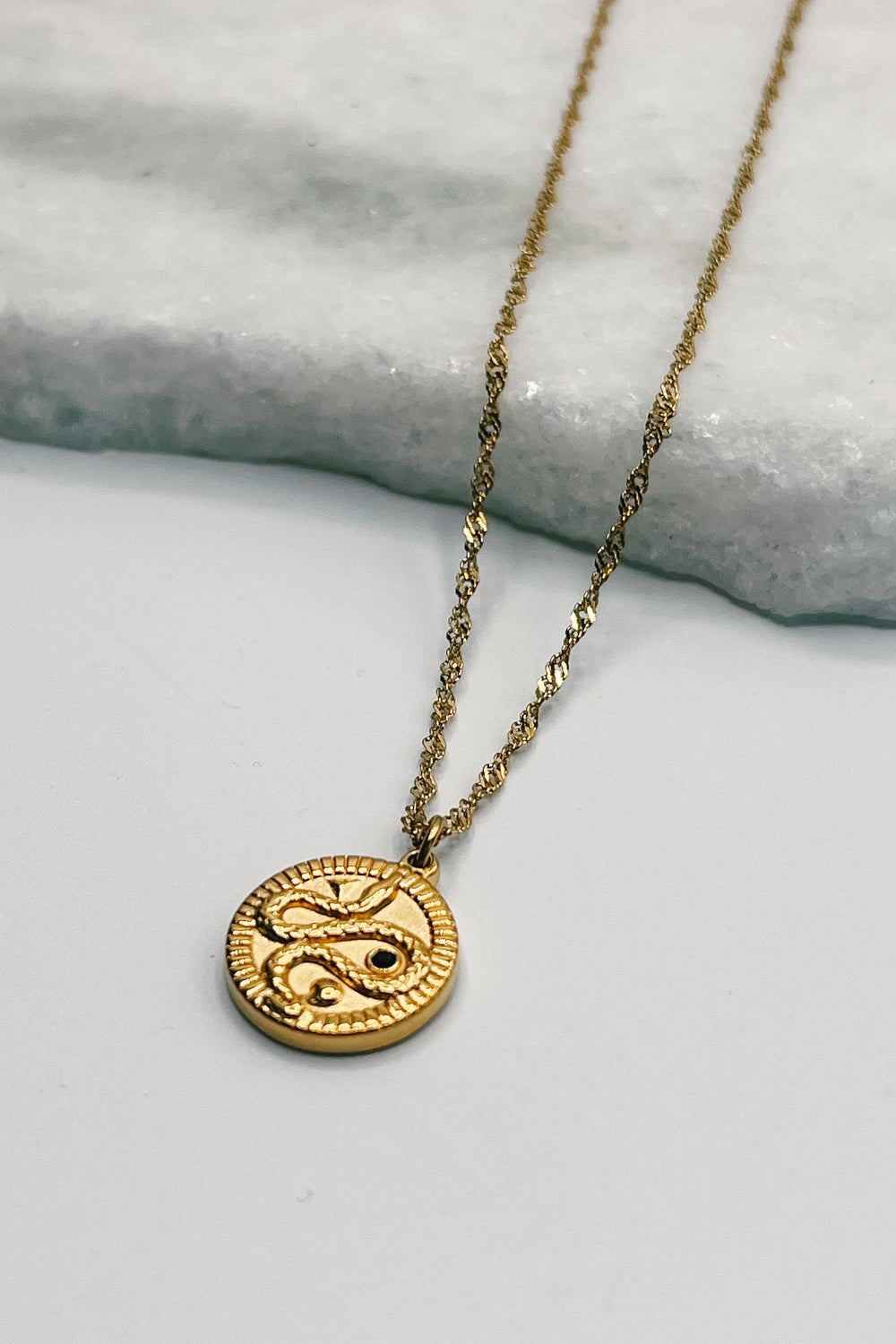 Image shows Samara Gold Snake Medallion Necklace against a white background. Necklace has a gold chain and a circle gold pendant that has a snake on it.