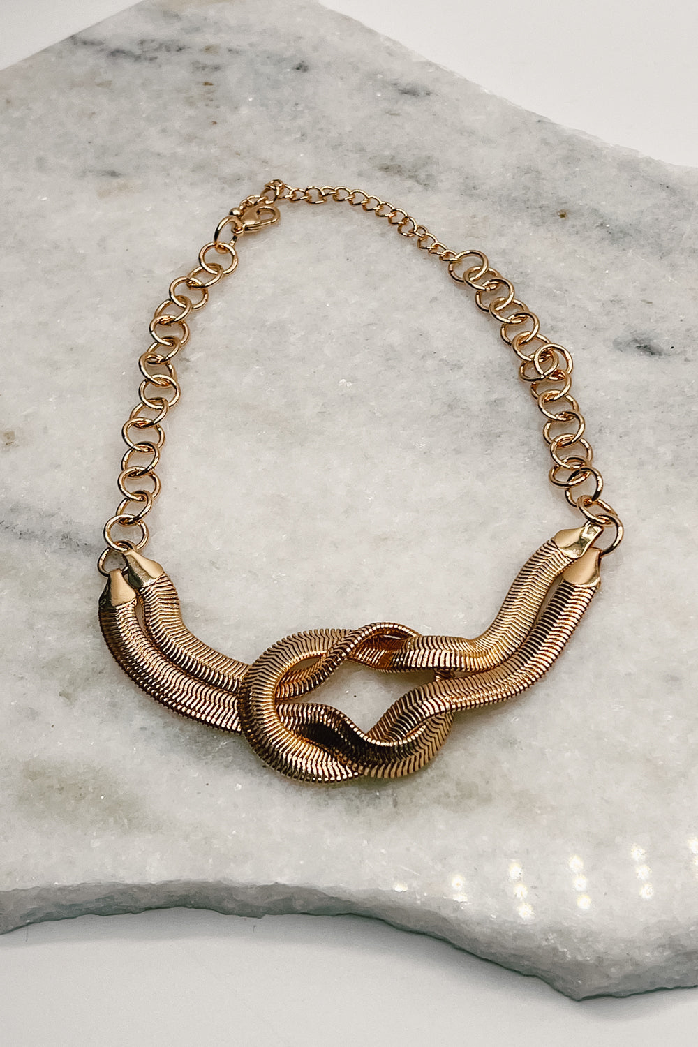 The Kora Knot necklace lies on a neutral background. (Alt. view)