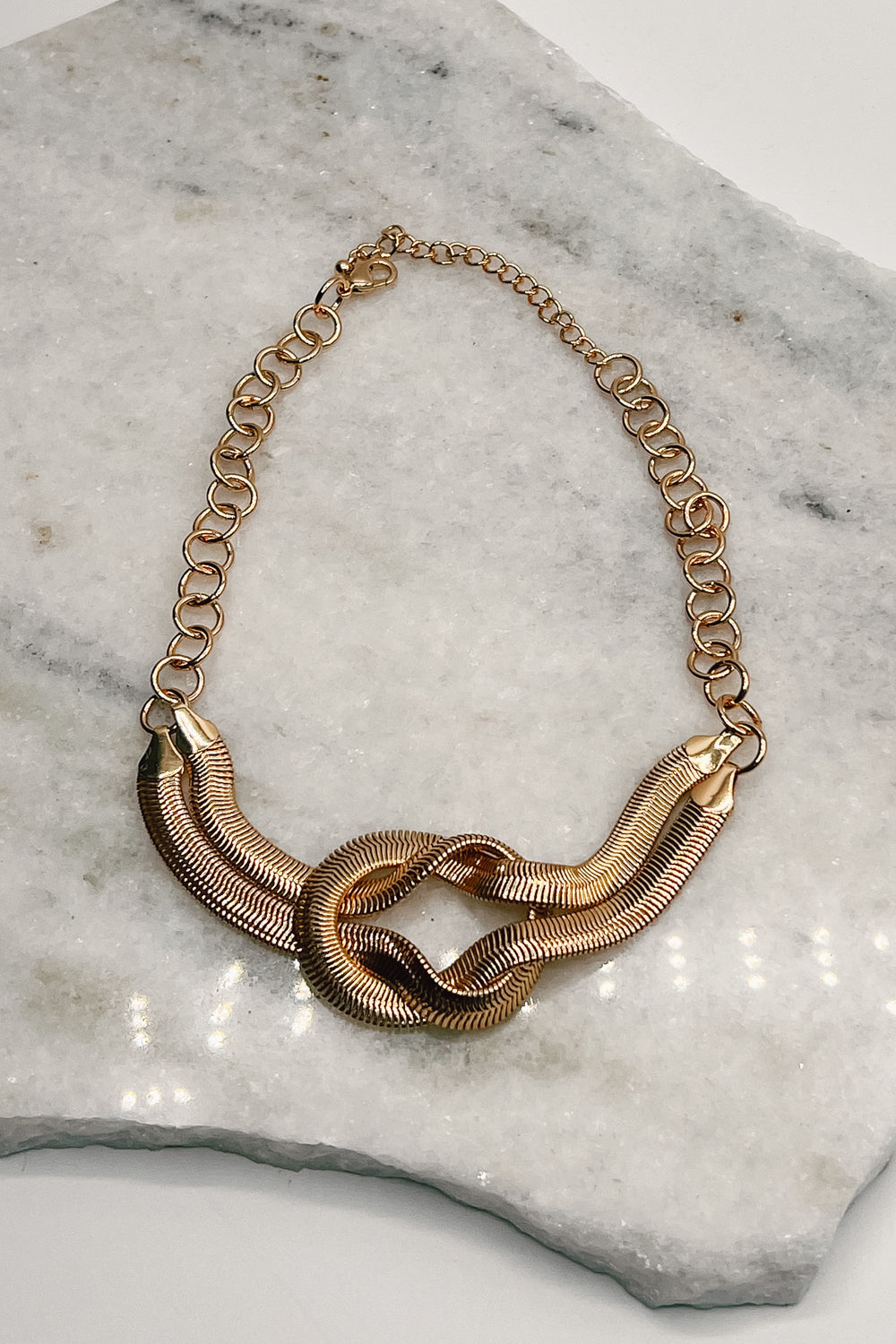 The Kora Knot Necklace lies on a neutral background.