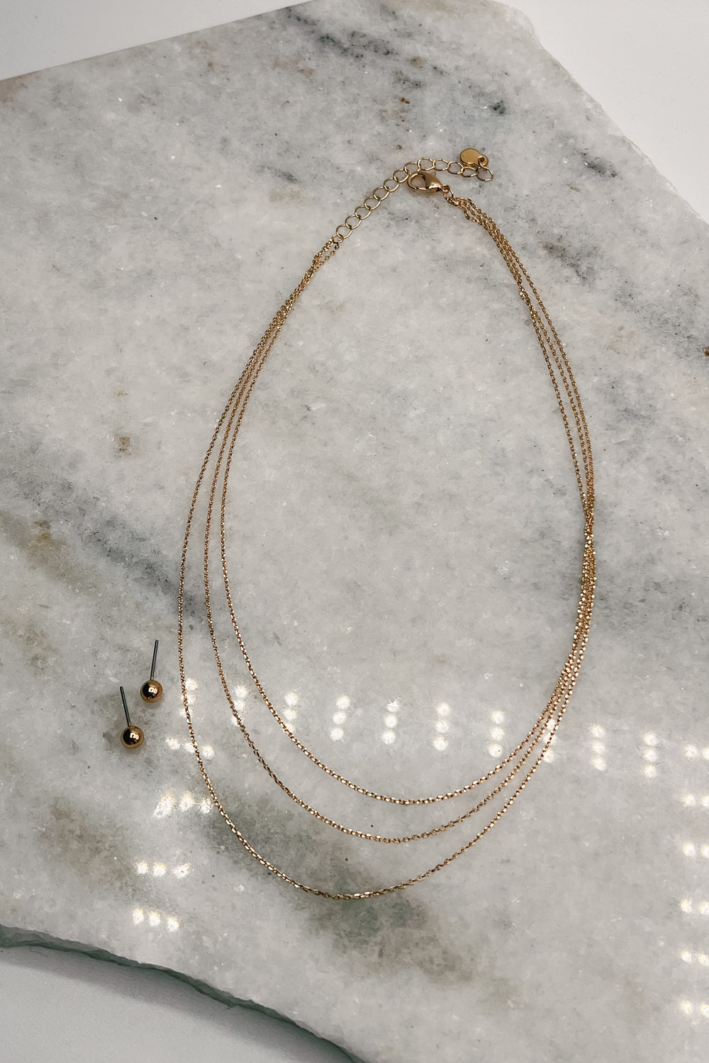 flat lay view of the Sloane Gold Layered Necklace & Earring Set which features layered gold chain necklace with gold studs