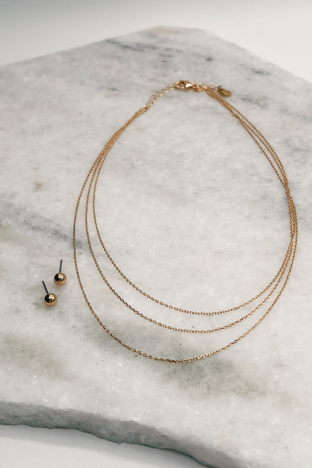 flat lay view of the Sloane Gold Layered Necklace & Earring Set which features  layered gold chain necklace with gold studs