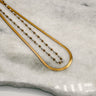 image shows the Ophelia Gold & Pearl Layered Necklace against a white marble background. Necklace has two layers- one gold chain and one with gold and white pearl beads