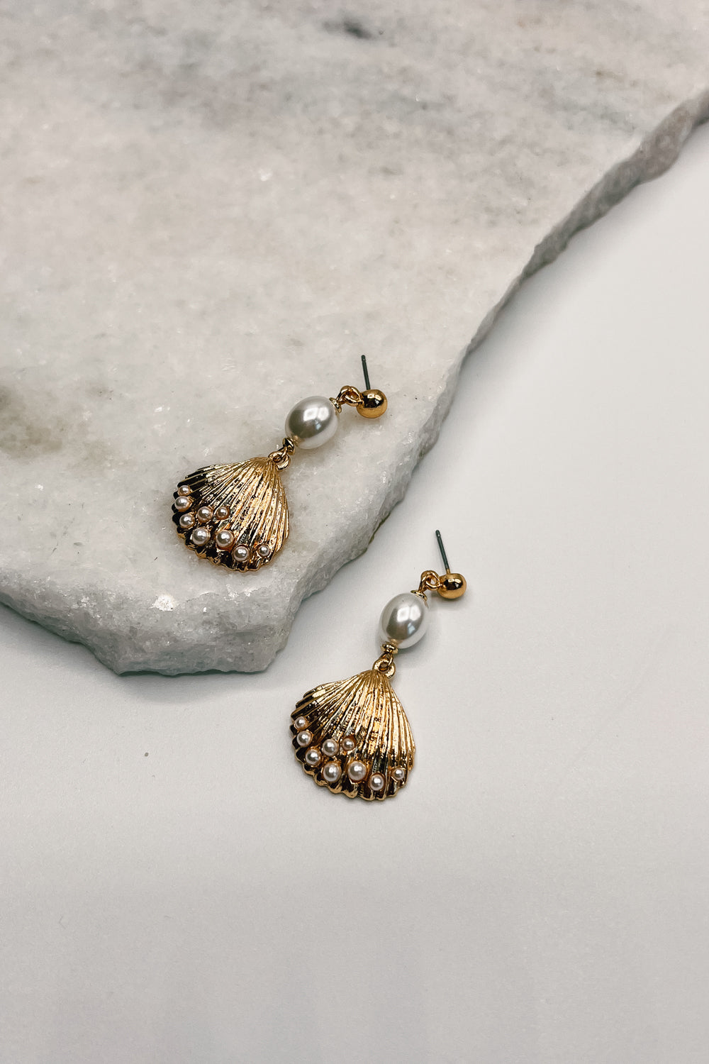 Alternate close up view of the Maris Shell earrings. The Maris earrings feature pearls and a gold seashell charm.