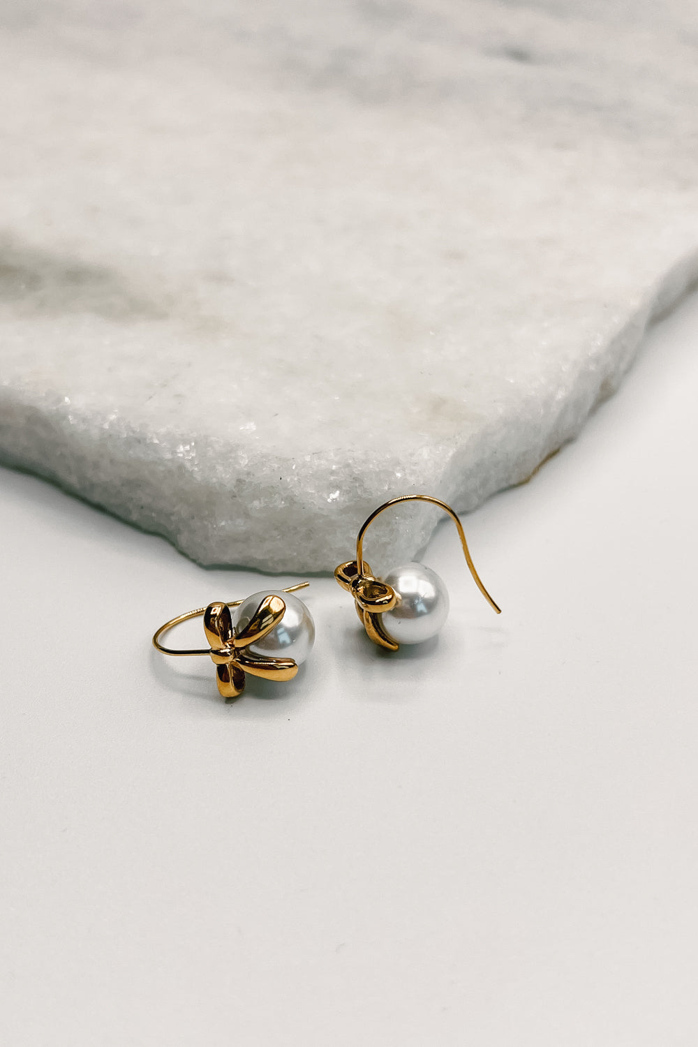 flat lay view of the Lara Pearl & Gold Bow Earring which features small gold dangle earrings with pearl and bow detail