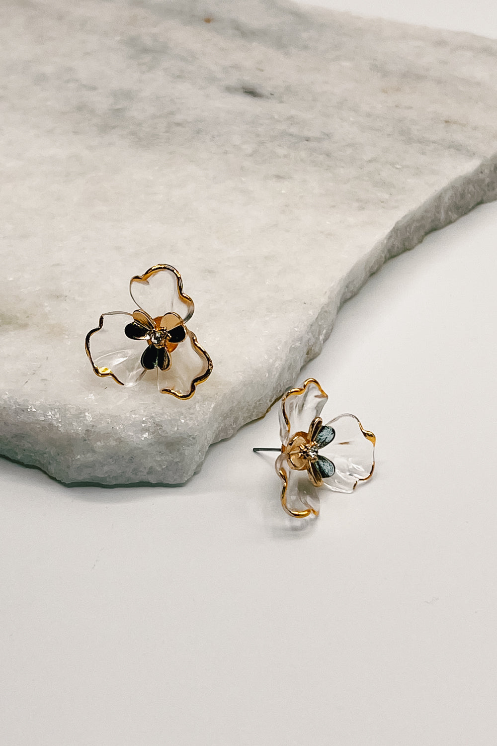 The flora earrings are seen up close lying on a neutral background.