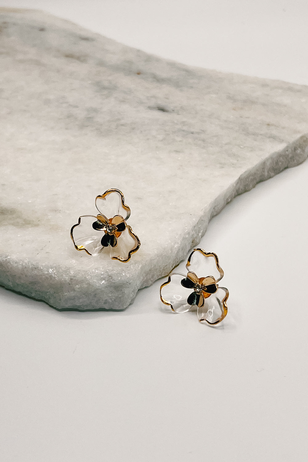 The flora earrings are seen up close lying on a neutral background.