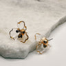 The flora earrings are seen up close lying on a neutral background.