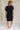 full body back view of female model wearing the Elsie Ribbed Short Sleeve Mini Dress which features Ribbed Fabric, Mini Length, Left Front Chest Pocket, Short Sleeves and Round Neckline. the dress is available in black and blue.
